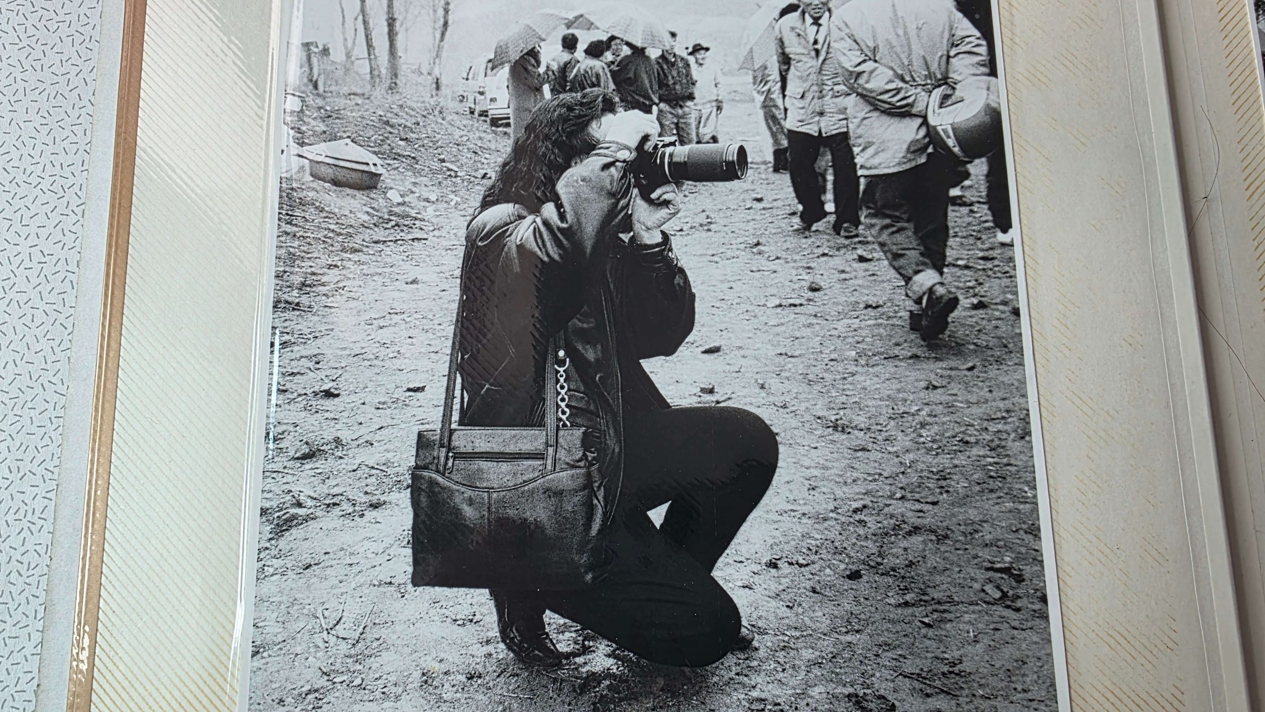 A young journalist kneeling on the ground, taking a photo in the field, captured in black and white