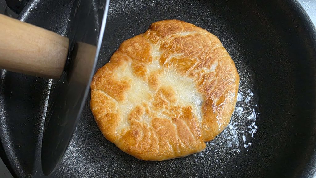 hotteok dough being pressed on a pan with oil and golden texture forming