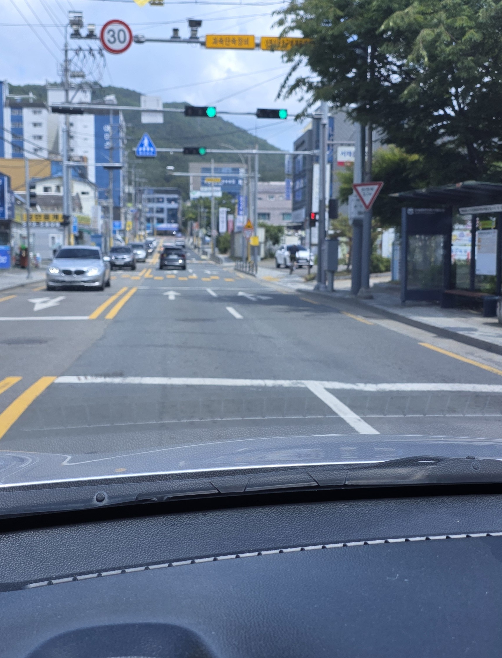 A quiet road intersection with an unclear stop line viewed from inside a car, with traffic lights, distant mountains, and a subtle feeling of hesitation.