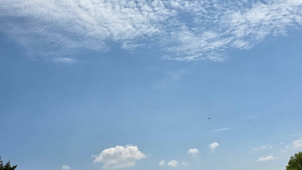 tiny fighter jet appearing as a small dot in a wide blue sky above a highway rest stop