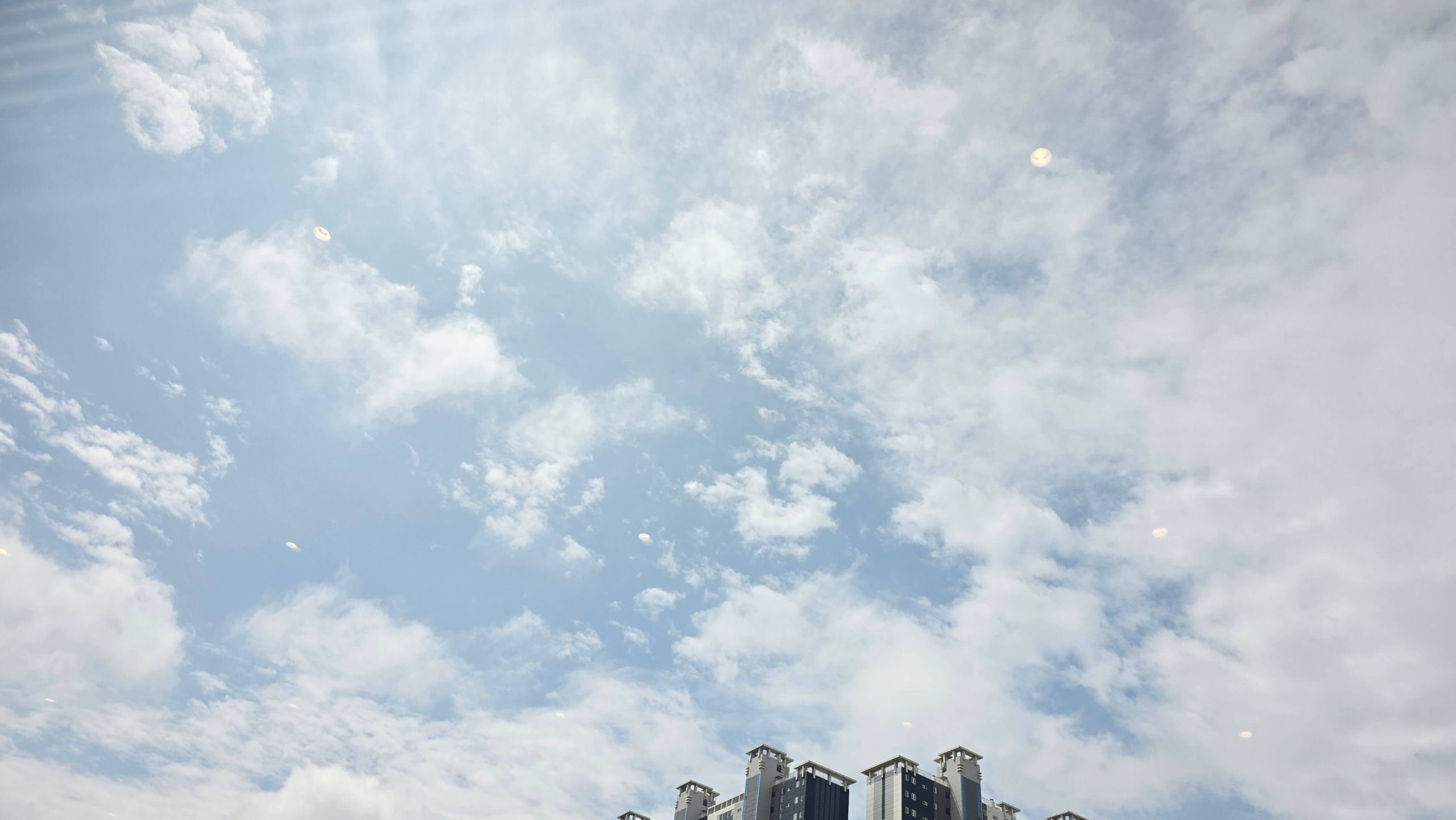Blue sky with scattered clouds above apartment buildings.