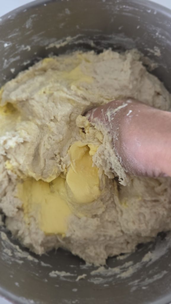 Hand-folding bread dough with butter in a mixing bowl