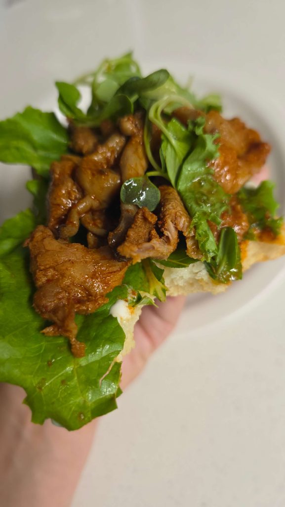 Homemade bread topped with spicy pork, lettuce, mushrooms, and baby greens