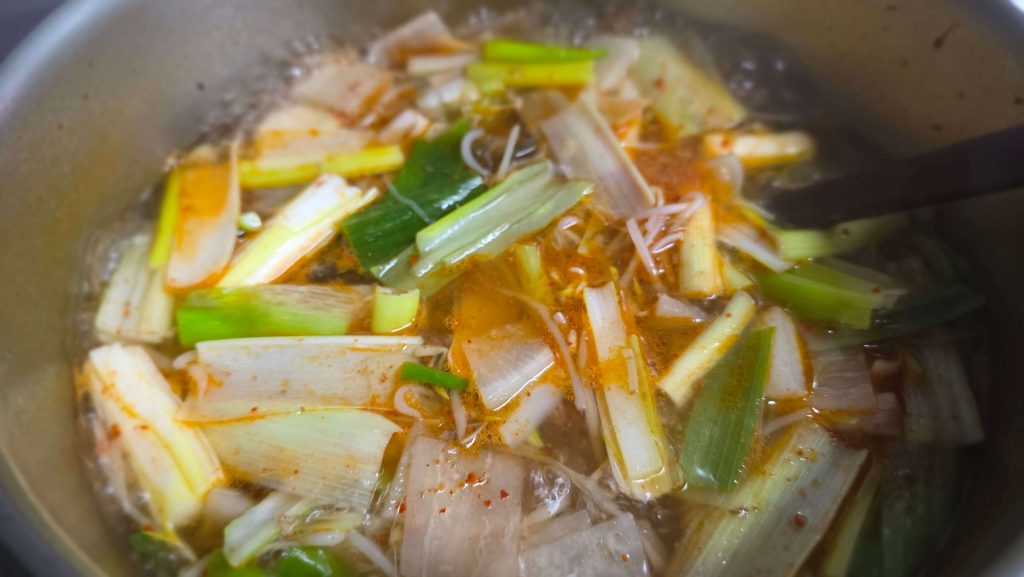 Spicy beef soup cooking with radish, bean sprouts, and green onions