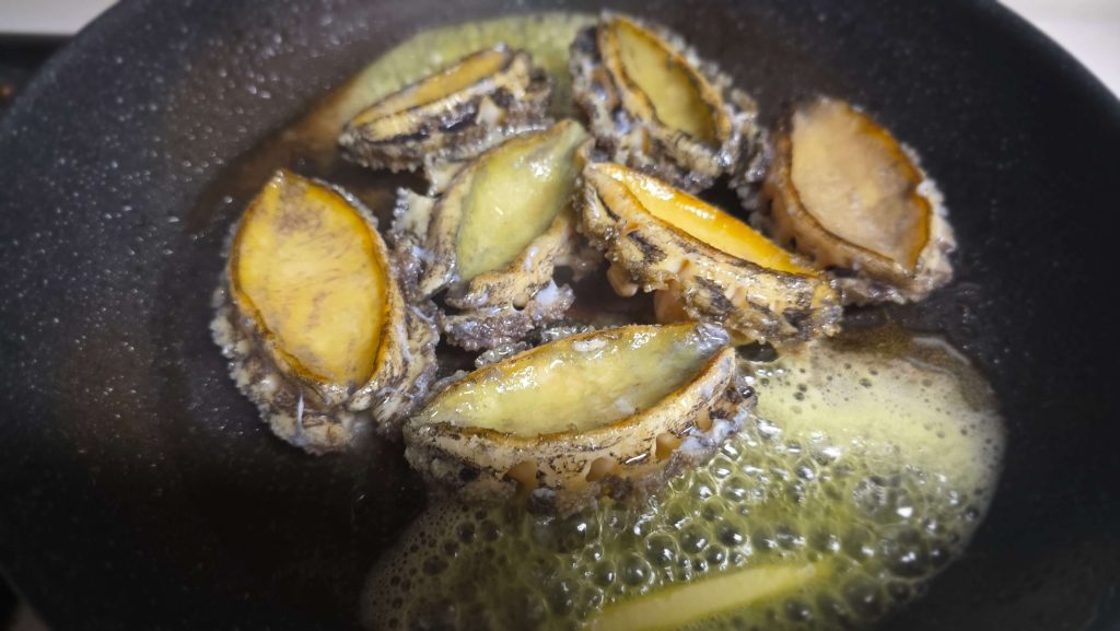 Fresh abalone cooking in melted butter in a frying pan