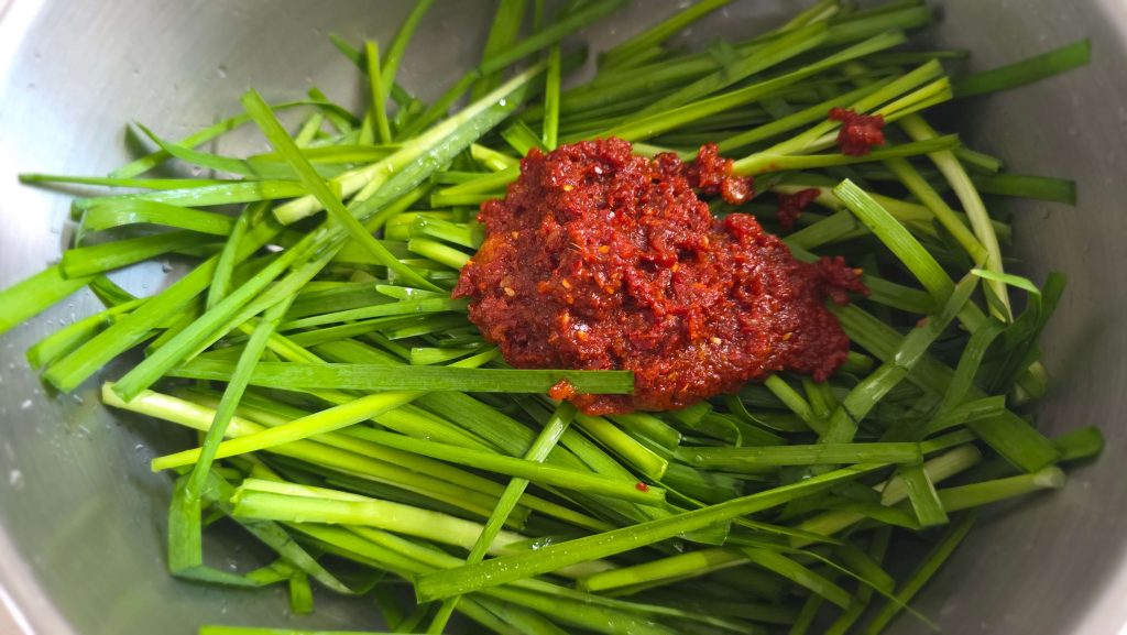 Fresh chives with kimchi seasoning in a mixing bowl