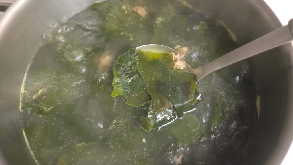 A ladle lifting seaweed from a pot of homemade Korean seaweed soup