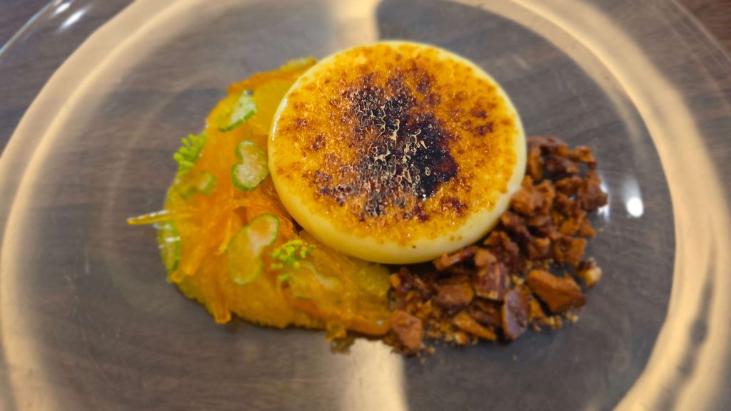 Citrus brûlée with a caramelized top, citrus fruit, and crunchy nut crumble on a glass plate