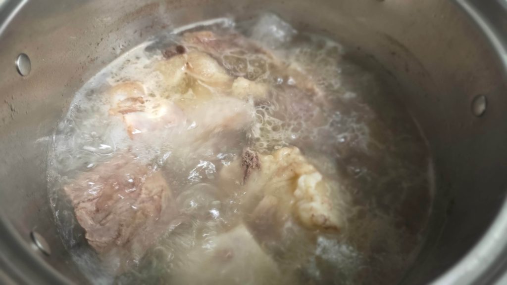 Beef bones and brisket boiling in a large stockpot with water only halfway up.