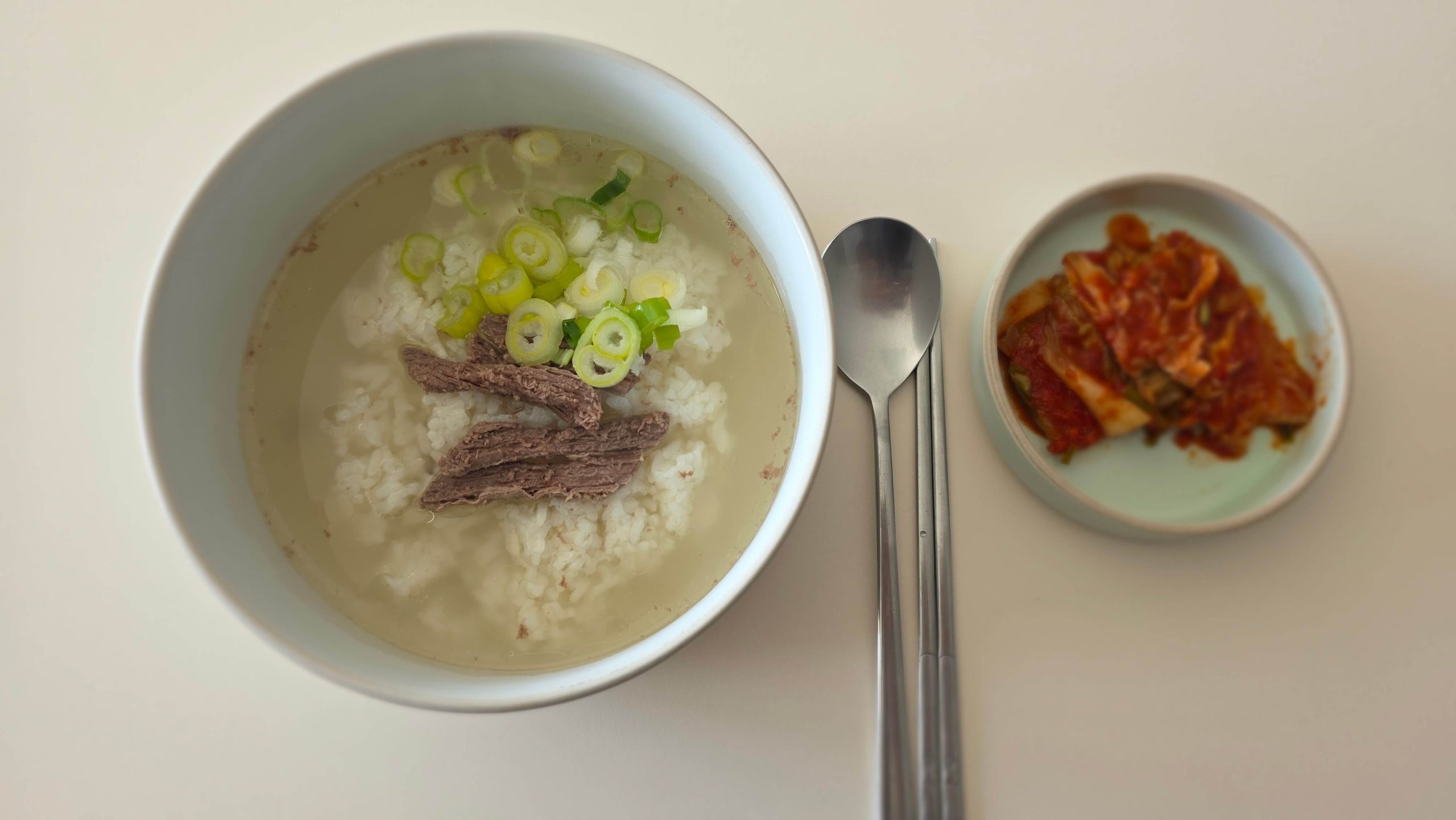 A bowl of Korean beef bone soup with rice, sliced brisket, and green onions, served with kimchi.