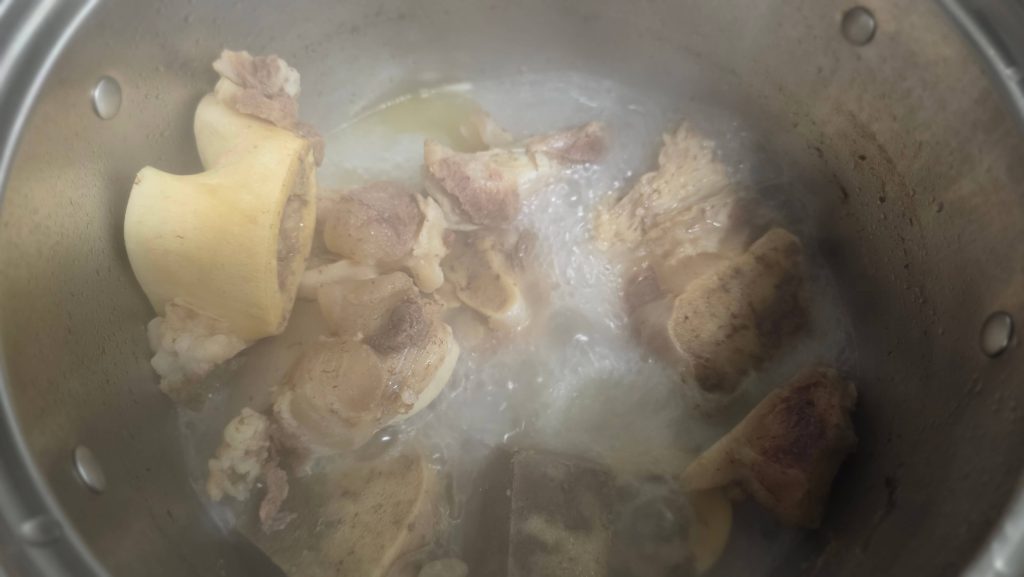 Beef bones exposed above the reduced, milky broth in a large stockpot.
