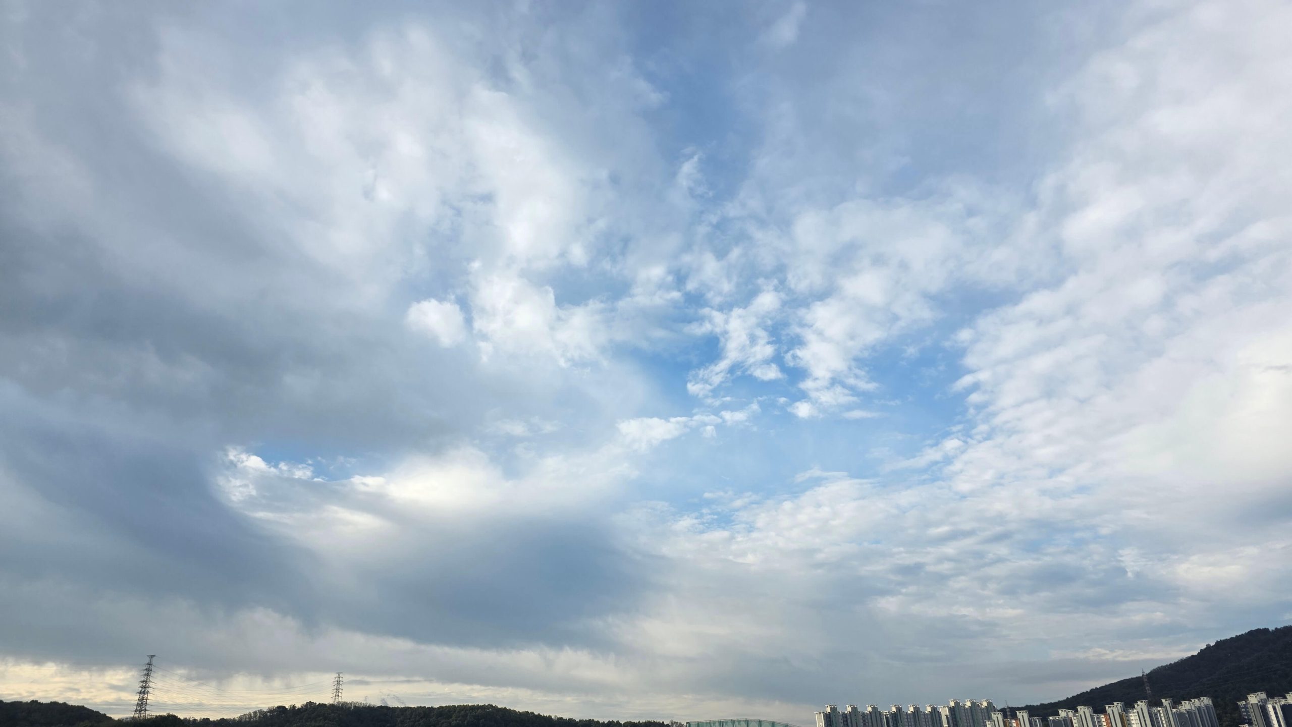 A wide blue sky with layers of gray and white clouds above the hills in Daegu.