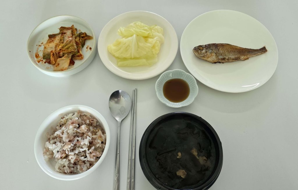 Homemade Korean lunch with seaweed soup, multigrain rice, grilled yellow croaker, steamed cabbage, and kimchi.