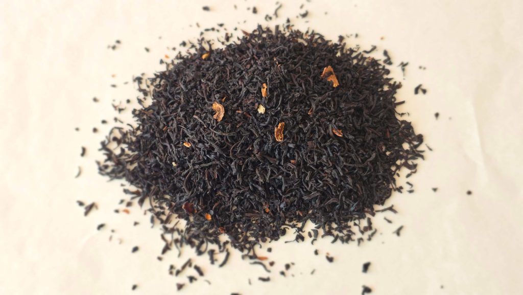 Loose black tea leaves mixed with small pieces of dried strawberry on a light background.