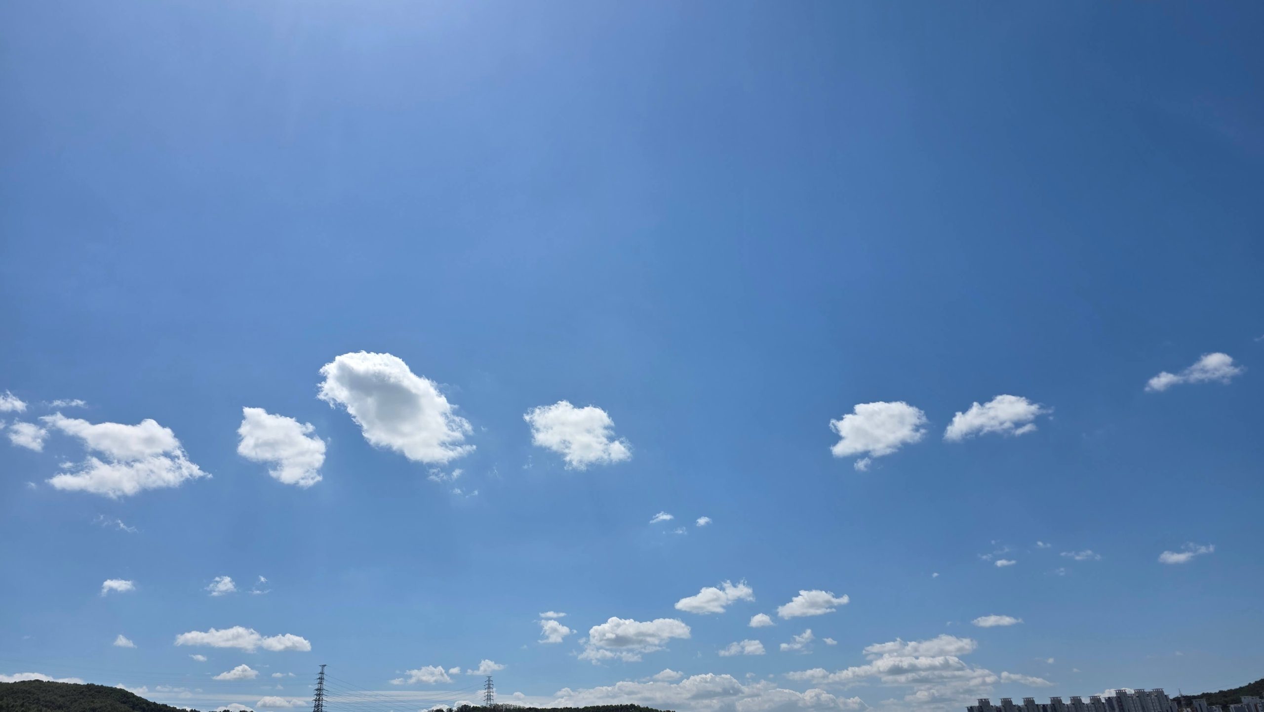 A bright blue sky with a row of similar white clouds drifting above the hills