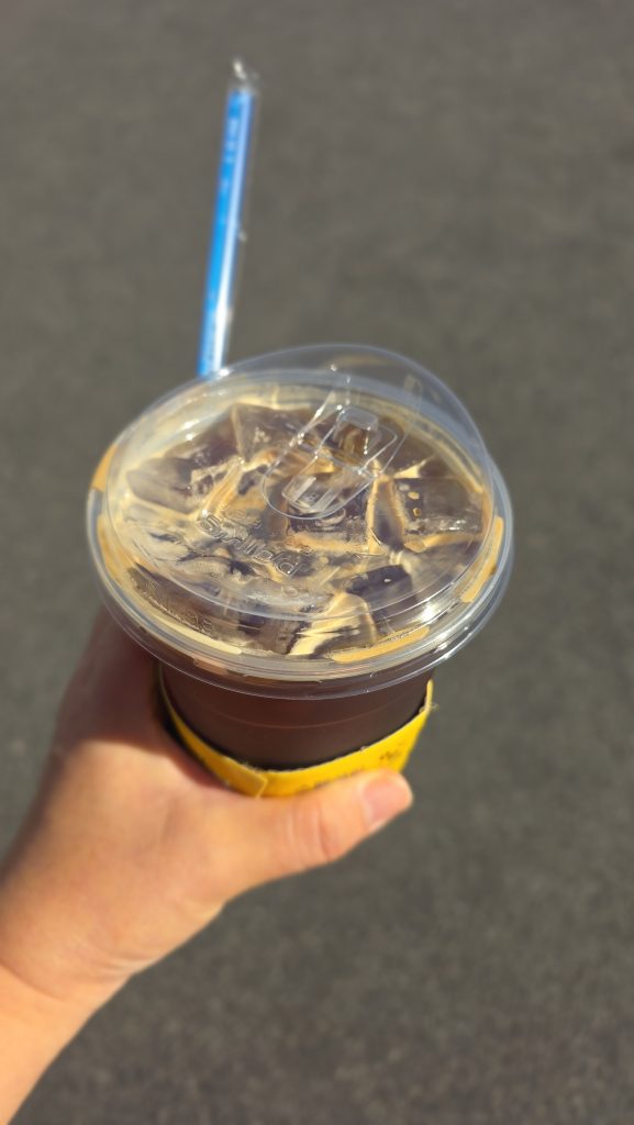 A hand holding a takeaway iced Americano in the sunlight.
