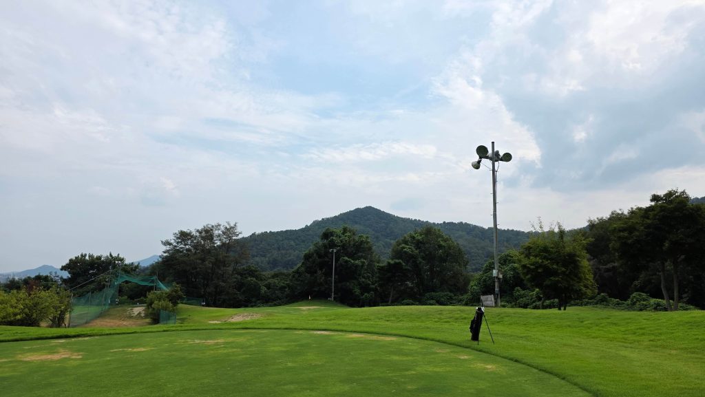 A green at the par-3 golf course surrounded by trees and hills