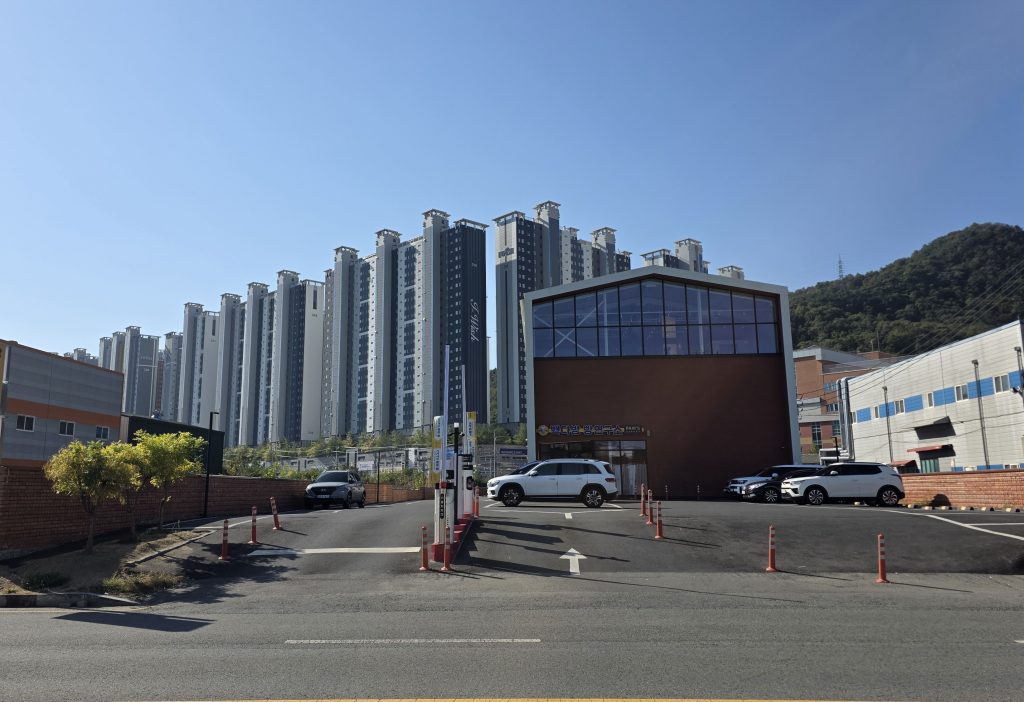 A large cafe with glass windows, seen from the road with apartment buildings and a green hill behind it.