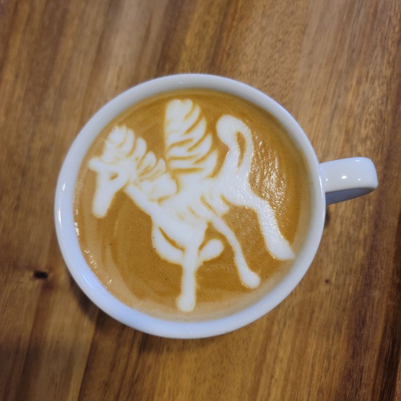 A Pegasus design created with milk foam on a cup of latte, resting on a wooden table.
